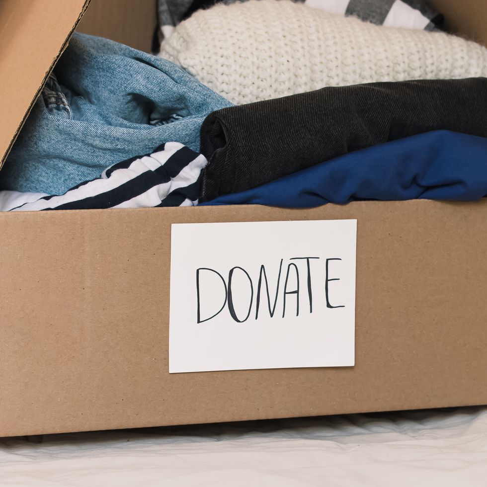 swedish death cleaning, woman's hands holding a box full of clothes to donate